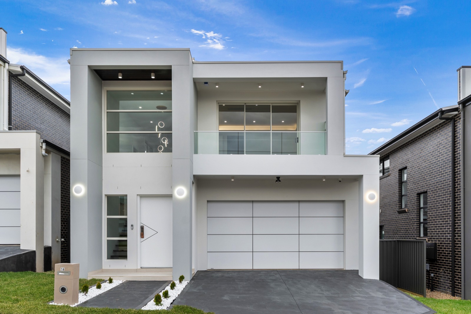 Two-storey contemporary white home with double garage beneath a clear blue sky